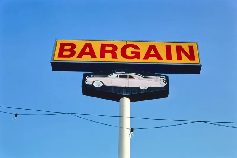Roadside BARGAIN sign above a classic car-shaped sign against a blue sky