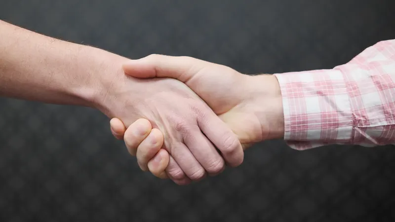 Two people shaking hands in close-up against a dark textured background